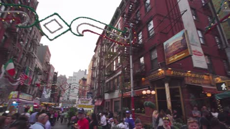 NYC:-Little-Italy-street-market-at-an-intersection,-in-the-middle-of-a-crowd-surrounded-by-food-stalls-and-games---Gimbal-pan-around---New-York-City,-USA