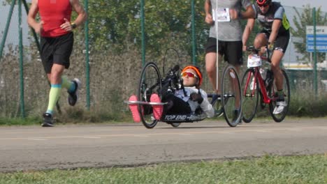 Disabled-Athlete-training-with-her-Hand-bike-with-Cyclist-and-Runners-Close-to-her