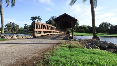 Golfwagen-Fährt-über-überdachte-Brücke,-Während-Die-Kamera-Von-Links-Nach-Rechts-Auf-Einem-Wunderschönen-Golfplatz-In-Florida-Schwenkt