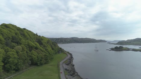 Aerial-shot,-approaching-Oban-bay-from-Dunollie-woods,-following-the-road-along-the-sea-side