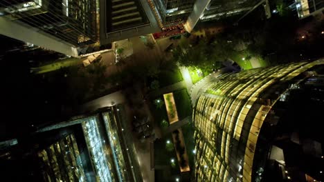 Spiral-overhead-view-of-modern-buildings-illuminated-at-night,-Nueva-Las-Condes,-financial-district-of-Santiago,-Chile