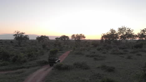 Drohne-Folgt-Safarifahrzeug,-Das-Bei-Sonnenaufgang-Auf-Unbefestigter-Straße-Im-Afrikanischen-Buschland-Fährt