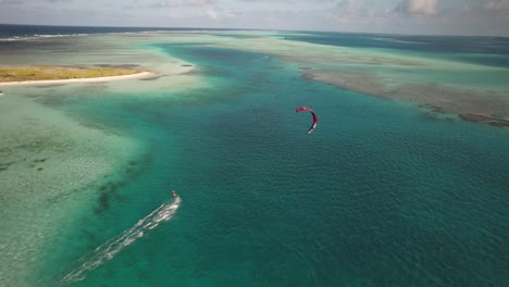 Aerial-drone-view-of-a-red-kite-surfer-on-a-turquoise-sea,-sunny-day,-tropical-vibe,-from-above
