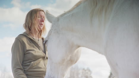 Vínculo-Entre-Una-Mujer-Y-Un-Caballo-Blanco-Mientras-Ella-Besa-El-Hocico,-Terapia-Equina