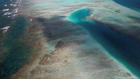 Aerial-tilt-up-reveal-of-Este-de-Coral-Cayo-Vapor-barrier-in-Los-Roques,-showcasing-the-vibrant-marine-life-and-crystal-waters