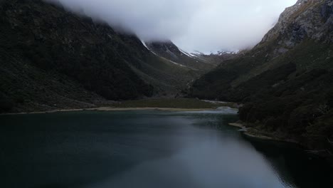 Vertical-drone-flight-capture-a-lake-in-the-middle-of-mountains-covered-by-clouds