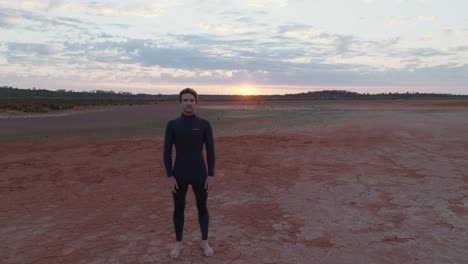 Male-model-with-dark-hair,-wearing-wetsuit,-stood-facing-camera-in-Austrailan-outback-desert