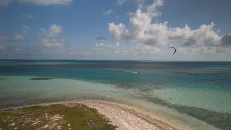 Aerial-shot-of-a-kitesurfer-with-a-red-kite-on-Cayo-Vapor,-turquoise-waters-under-sunny-skies
