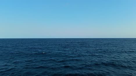Aerial-pullback-above-calm-ocean-with-small-white-caps-on-top-and-soft-blue-gradient-sky-horizon