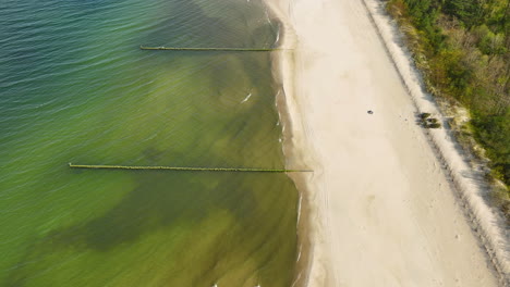 Aerial-view-of-a-serene-beach-clear-demarcation-between-the-sandy-shore-and-the-shallow-waters,-with-two-jetties-extending-into-the-sea,-highlighting-the-tranquil-and-undisturbed-natural-setting