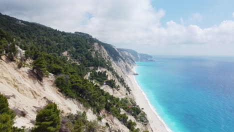 A-drone-emerges-from-the-forest-along-the-coast-of-Egremni-Beach-in-Lefkada,-Greece