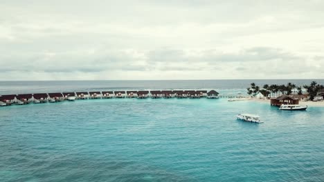 Drone-video-of-a-tropical-resort-in-the-Maldives,-blue-lagoon-reef,-sunny-weather,-turquoise-shallow-water,-water-villas,-island-port,-4K
