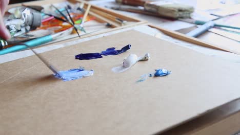 Skilled-artist-hand-mix-oil-paint-blue-shades-on-studio-table-with-brushes-and-tools