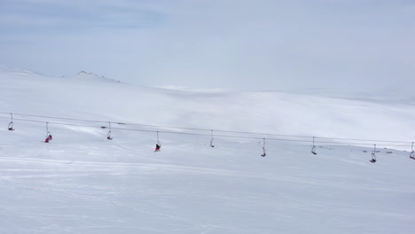 Aerial-view-drone-tracking-following-skiers-in-ski-lifts-heading-to-mountain-peak-on-ski-resort-panning-left-Kaimaktsalan-Greece
