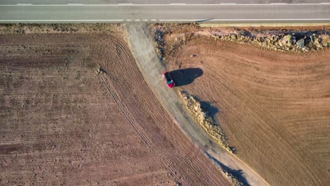 Red-car-standingon-a-dirt-road-through-golden-fields-in-Lleida,-Catalonia,-aerial-view