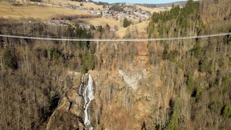 Walking-bridge-over-waterfalls-with-a-town-visible-in-the-background-during-an-autumn-day