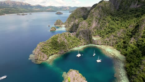 Vista-Desde-Drones-De-Una-Hermosa-Bahía,-Aguas-Azules,-Montañas-Verdes-Y-Catamaranes-Flotantes