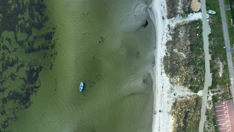 Aerial-view-capturing-a-solitary-boat-on-clear,-shallow-waters-near-a-white-sandy-shore,-contrasting-with-vibrant-underwater-plant-life