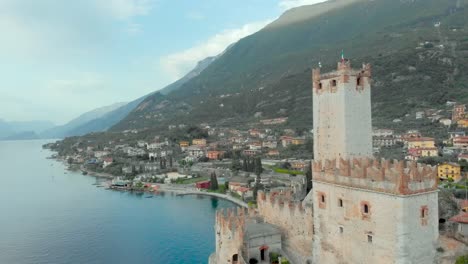 Drone-footage-unveiling-the-tower-of-Malcesine-Castle-on-Lake-Garda,-Italy,-showcasing-tourism,-vacation,-nature,-water,-blue-sky,-and-greenery