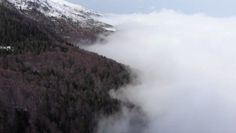 Vista-De-Drones-Del-Hermoso-Bosque-De-La-Ladera-Cubierto-De-Nubes-Flotantes-Pico-De-Montaña-Cubierto-De-Nieve-A-Lo-Lejos-Día-De-Invierno-Kaimaktsalan-Grecia