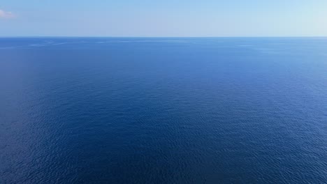 Panoramic-aerial-descend-to-Caribbean-sea-ocean-water-surface-with-light-blue-sky-on-horizon