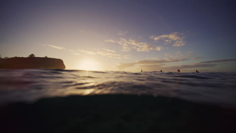 Water-spills-off-front-as-sunlight-casts-morning-light-across-surfers-at-break