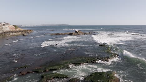 Fast-aerial-push-in-of-waves-crashing-on-rocks-over-the-blue-Pacific-Ocean-in-San-Diego,-California-on-a-sunny-day