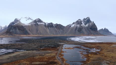 Schneebedeckte-Bergkette-Mit-Scharfen-Gipfeln-über-Der-Schwarzen-Sandstrand-Meeresbucht