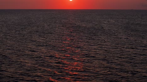 Aerial-pullback-tilt-up-reveals-beautiful-fire-red-orange-sunset-over-calm-serene-ocean-water