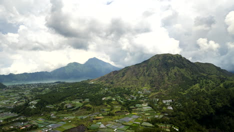 Monte-Batur-En-Movimiento-En-La-Nube,-Paisaje-Verde,-Edificios-Dispersos,-Hiperlapso.