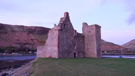 Scenic-landscape-view-of-historical-Lochranza-Castle-landmark-ruins-during-beautiful-twilight-sunset-on-Isle-of-Arran-in-Western-Scotland-UK