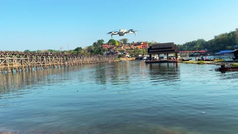 A-DJI-Mini-4-drone-hovers-stationary-above-the-Kwai-Yai-River-and-the-iconic-Mon-Bridge-in-Kanchanaburi,-Thailand,-capturing-breathtaking-aerial-footage