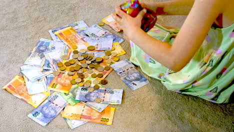 Girl-dumps-coins-from-money-box-onto-spread-out-South-African-banknotes