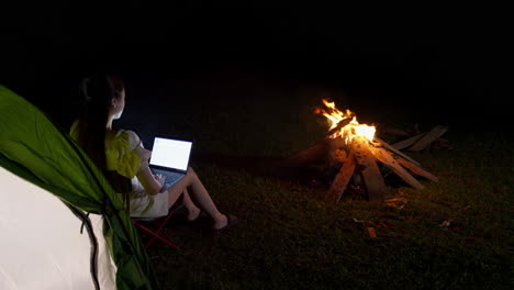 young-woman-stay-connected-in-remote-area-while-camping-outdoor-at-night-working-on-laptop-in-front-of-bonfire