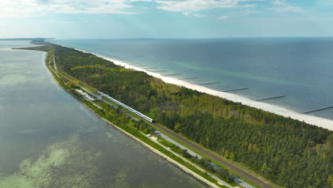 Eine-Spektakuläre-Luftaufnahme-Von-Kuźnica-Auf-Der-Halbinsel-Hel,-Ein-Zug-Fährt-Entlang-Des-Schmalen-Landstreifens,-Der-Von-Der-Bucht-Und-Der-Ostsee-Flankiert-Wird-Und-Die-Einzigartige-Geographie-Der-Gegend-Hervorhebt