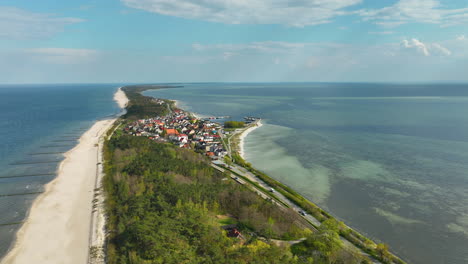 Aerial-view-of-Kuźnica,-Poland,-featuring-a-narrow-strip-of-land-bordered-by-the-sea-on-one-side-and-the-bay-on-the-other,-with-a-vibrant-community-nestled-between