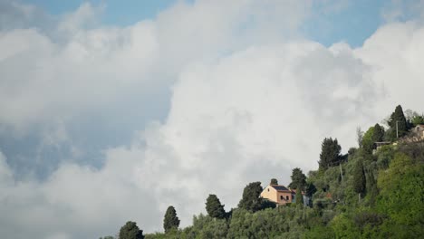 Hillside-villa-under-fast-moving-clouds-on-a-sunny-day,-timelapse