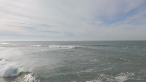 Orbiting-drone-shot-showing-group-of-surfer-in-Atlantic-Ocean-during-cloudy-day