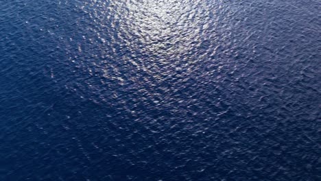 Sunlight-shimmers-in-rounded-ray-dissapearing-to-blue-on-top-of-Caribbean-ocean-water,-aerial