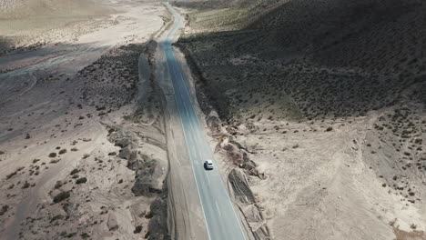 Drone-shot-of-lonely-car-traveling-on-asphalt-road-in-arid-mountainous-landscape-in-Salta,-Argentina