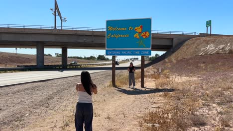 Young-tourists-taking-picture-with-Welcome-to-California-sign