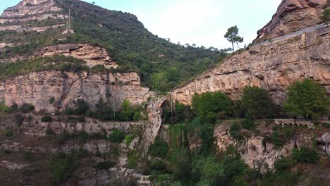 Sant-miquel-del-fai,-showing-lush-cliffs-and-a-waterfall-in-barcelona,-majestic-and-serene,-aerial-view