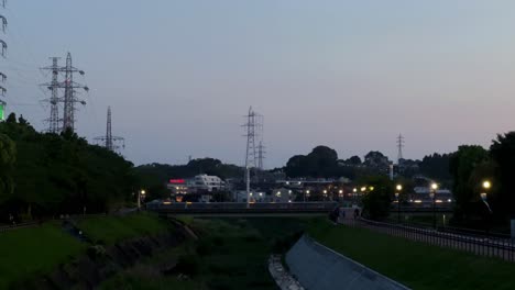 Twilight-scene-in-urban-park-with-illuminated-pathways-and-distant-city-lights,-people-walking