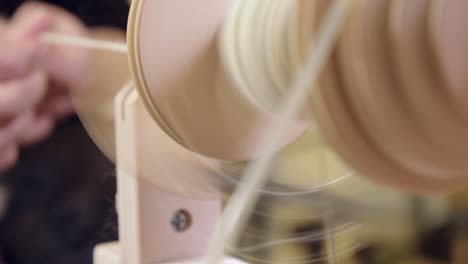 Defocused-hands-feed-wool-into-treadle-spinning-wheel-to-make-yarn