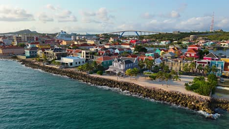 Dolly-Aéreo-Sobre-El-Agua-Del-Mar-Caribe-Se-Eleva-A-Los-Techos-Recortados-De-Color-Rojo-Anaranjado-De-Willemstad-Curacao