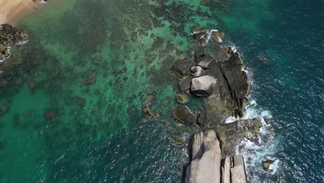 Slow-cinematic-drone-tilt-down-over-beautiful-rock-in-ocean-with-waves