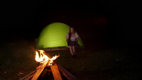 asiatic-woman-chatting-with-tablet-laptop-in-front-of-night-bonfire-while-camping-outdoor-at-night-in-remote-area