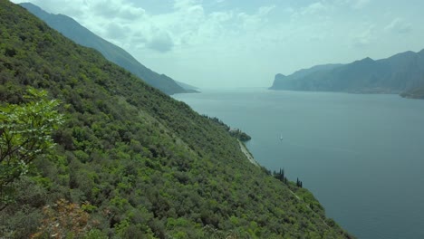 Panoramic-view-of-Lake-Garda-from-the-trekking-path-on-the-Busatte-mountain-in-Torbole,-amidst-a-backdrop-of-clear-skies,-clouds,-and-lush-vegetation,-showcasing-the-natural-beauty