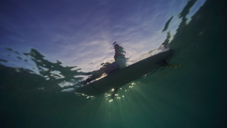Backlit-silhouette-of-surfer-sitting-on-longboard,-view-from-underwater