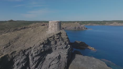 Torre-d'Es-Colomer-Blue-Mediterranean-skyline-drone-fly-Menorca-rocky-beach-stone-tower-viewpoint